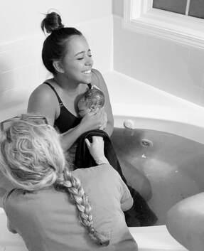 mom giving birth in birthing tub with midwife's assistance during water birth