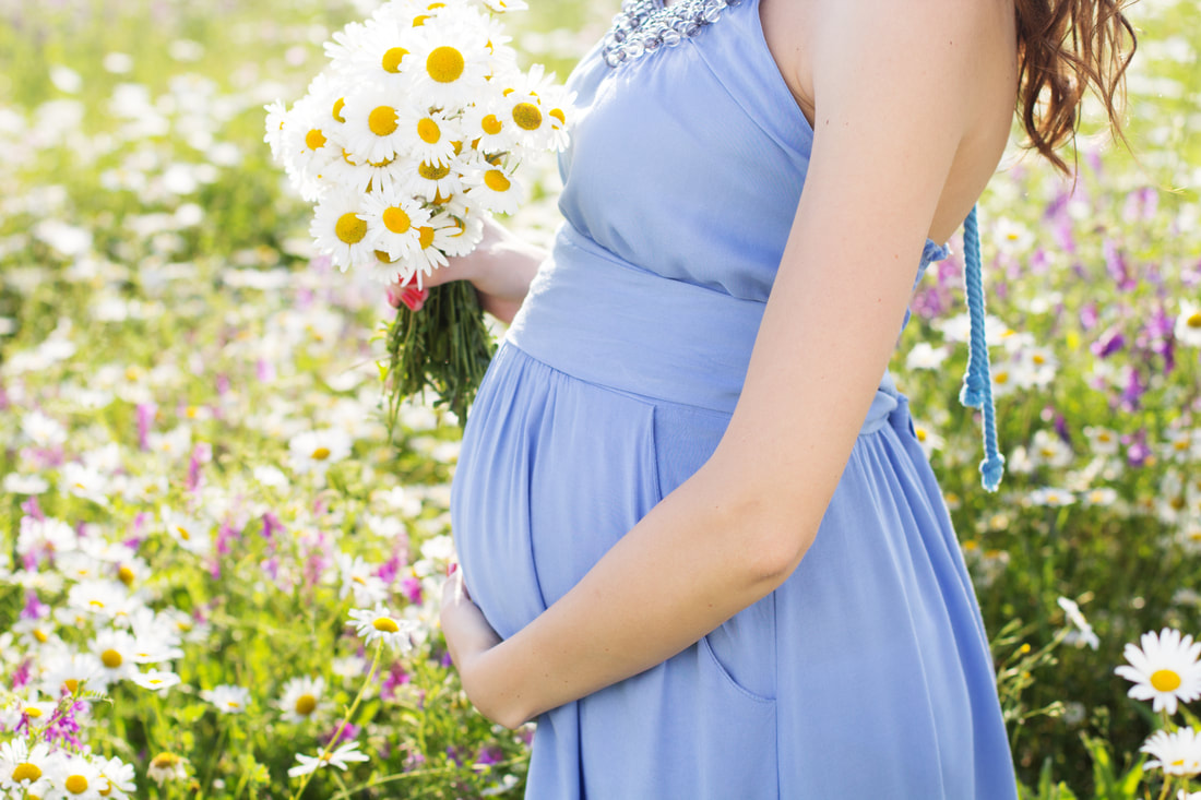 pregnant mom holding belly in field of wildflowers